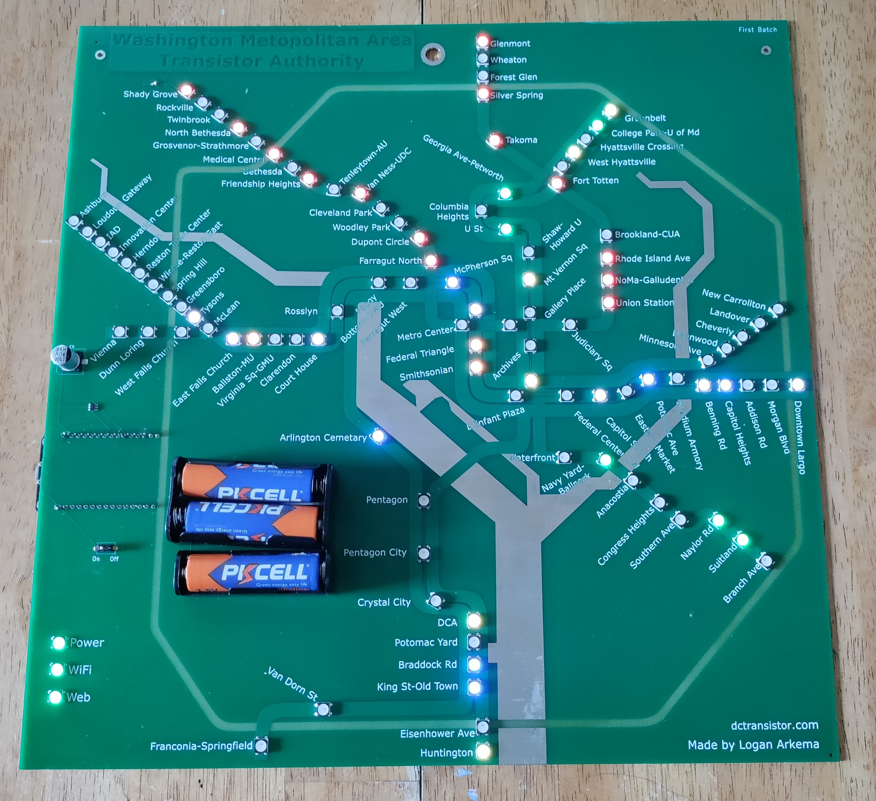 Large picture of a DCTransistor board, powered on to show live train positions. The board is programmable circuit board, mostly light green except for a dark green title and dark green rectangles representing the DC metro train lines, a beige boundary representing the beltway, and silver representing the Potomac and Anacostia rivers. It is designed to represent the DC Metro System map.